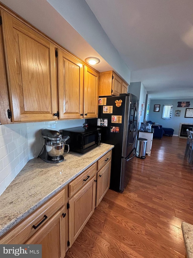 kitchen with light stone countertops, hardwood / wood-style flooring, black appliances, and backsplash