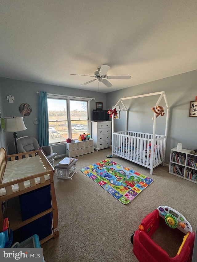 bedroom featuring a nursery area, ceiling fan, and carpet