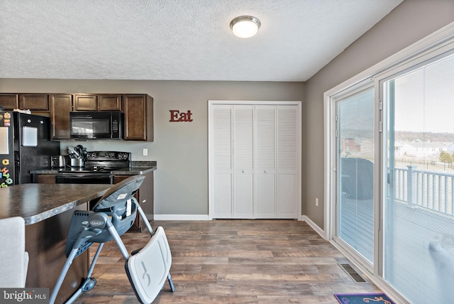 kitchen with hardwood / wood-style flooring, dark brown cabinetry, a textured ceiling, and black appliances