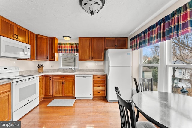 kitchen featuring white appliances, light countertops, a textured ceiling, light wood-type flooring, and a sink