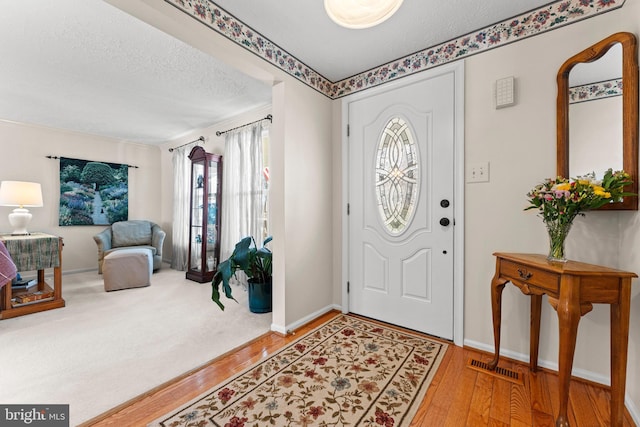 foyer entrance with visible vents, a textured ceiling, baseboards, and wood finished floors