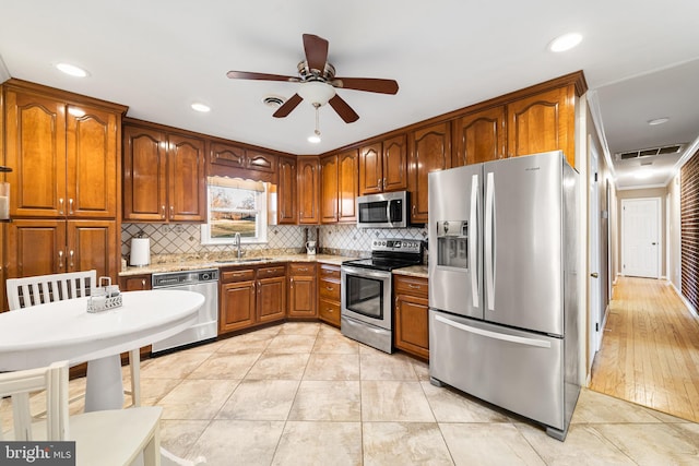 kitchen with tasteful backsplash, visible vents, appliances with stainless steel finishes, brown cabinets, and a sink