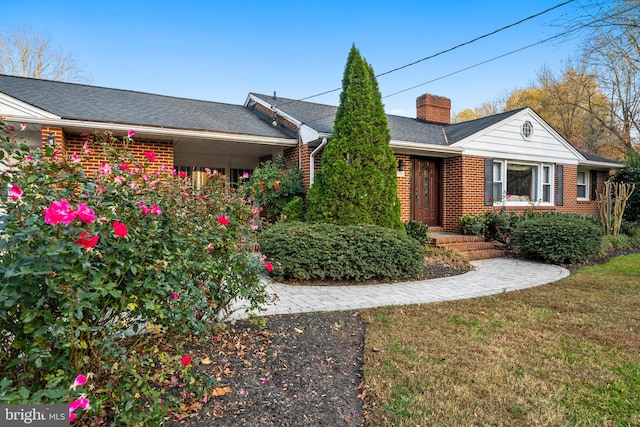 ranch-style home featuring roof with shingles, brick siding, a chimney, and a front lawn