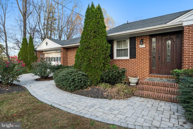 property entrance featuring a garage, brick siding, and a shingled roof