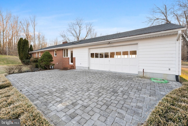 view of home's exterior with a shingled roof, a chimney, an attached garage, decorative driveway, and brick siding