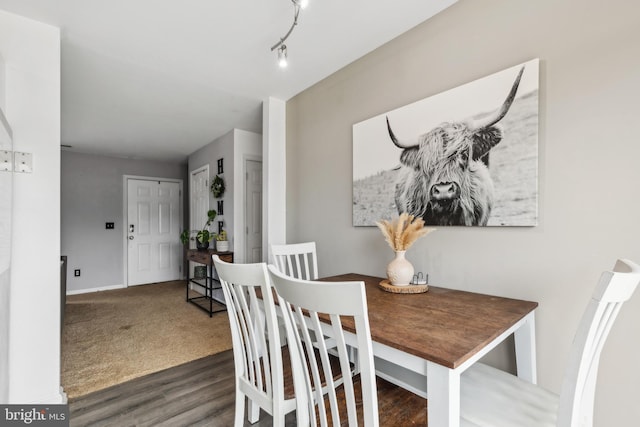 dining room featuring baseboards, dark wood finished floors, track lighting, and dark colored carpet