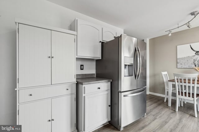 kitchen with white cabinets, dark countertops, light wood-style flooring, rail lighting, and stainless steel refrigerator with ice dispenser