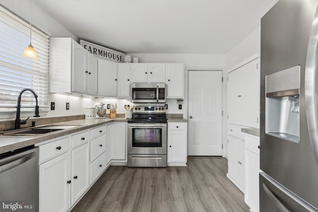 kitchen featuring a sink, white cabinetry, appliances with stainless steel finishes, dark countertops, and pendant lighting