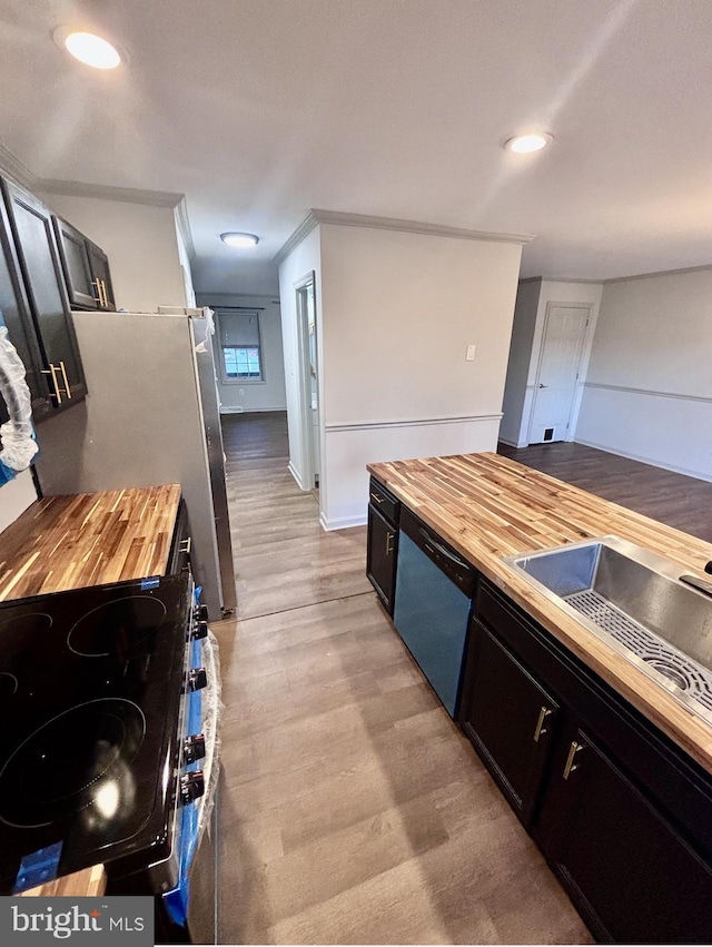 kitchen featuring sink, butcher block countertops, light wood-type flooring, ornamental molding, and appliances with stainless steel finishes