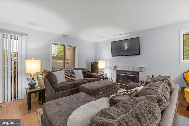 living room with a tile fireplace, plenty of natural light, wood finished floors, and visible vents