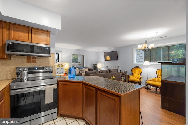 kitchen featuring dark countertops, brown cabinets, a peninsula, stainless steel appliances, and backsplash