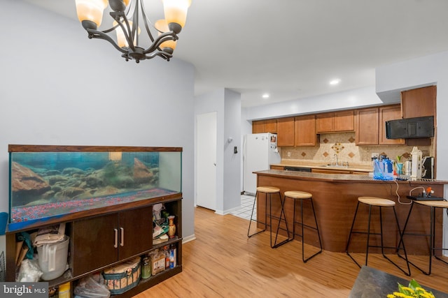 kitchen featuring a breakfast bar, dark countertops, freestanding refrigerator, and brown cabinets