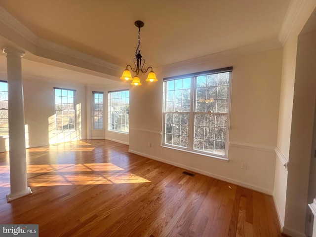 unfurnished dining area with decorative columns, hardwood / wood-style flooring, crown molding, and an inviting chandelier