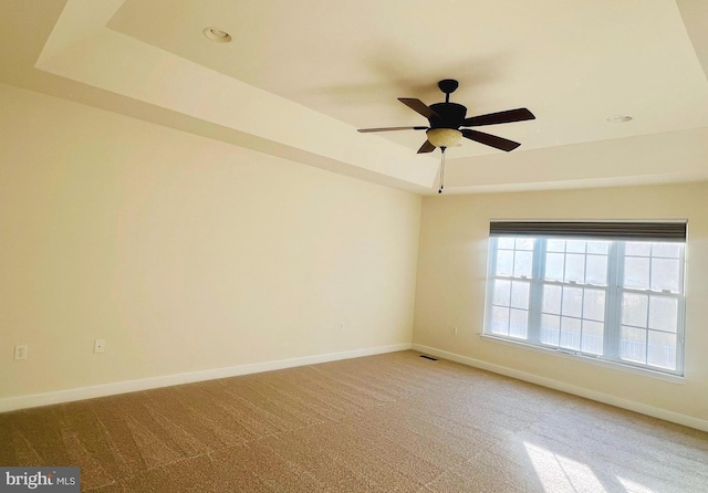 carpeted spare room featuring a tray ceiling and ceiling fan