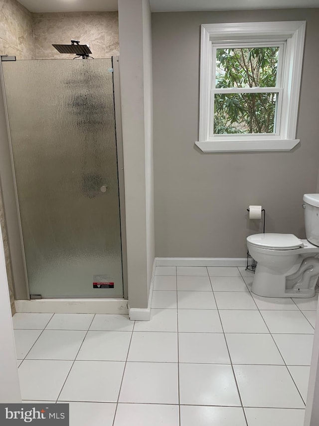 bathroom with a stall shower, tile patterned flooring, baseboards, and toilet