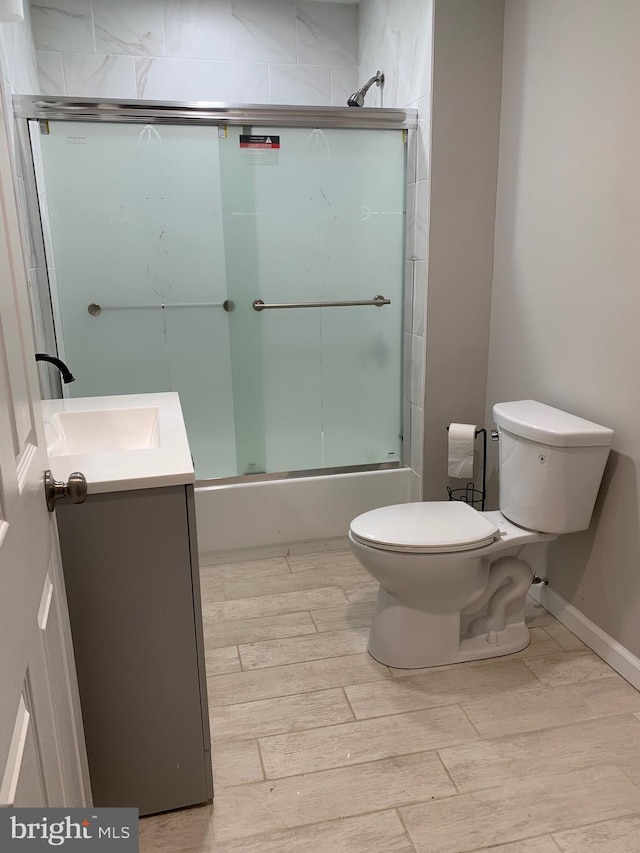 full bath featuring wood tiled floor, enclosed tub / shower combo, vanity, and toilet