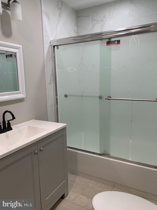 full bath with toilet, bath / shower combo with glass door, and vanity