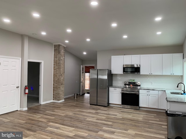 kitchen featuring decorative columns, stainless steel appliances, white cabinetry, a sink, and wood finished floors