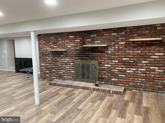 unfurnished living room with brick wall, a fireplace, wood finished floors, and baseboards