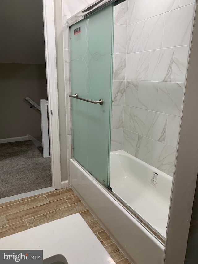 bathroom with wood tiled floor, baseboards, and combined bath / shower with glass door