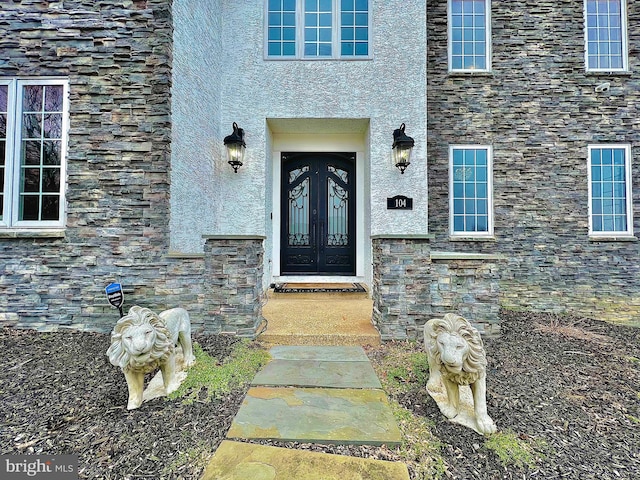 doorway to property with stone siding, french doors, and stucco siding