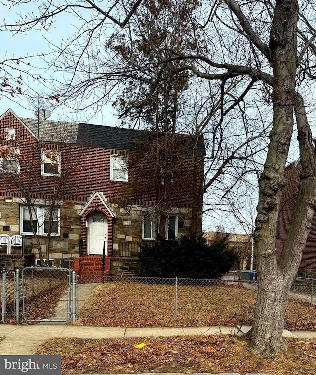 view of property featuring stone siding, brick siding, a fenced front yard, and a gate