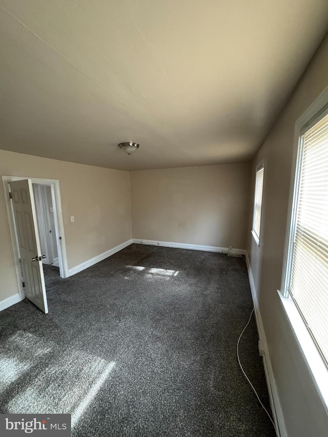 spare room with dark colored carpet and baseboards