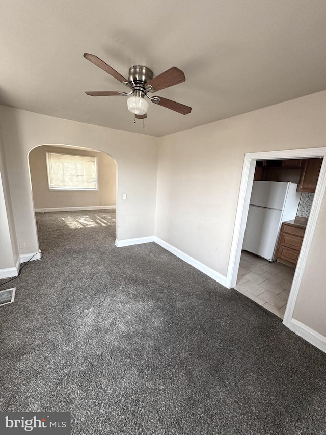 spare room featuring arched walkways, ceiling fan, carpet flooring, and baseboards