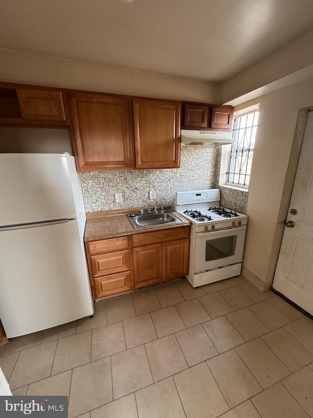 kitchen with white appliances, decorative backsplash, brown cabinets, under cabinet range hood, and a sink