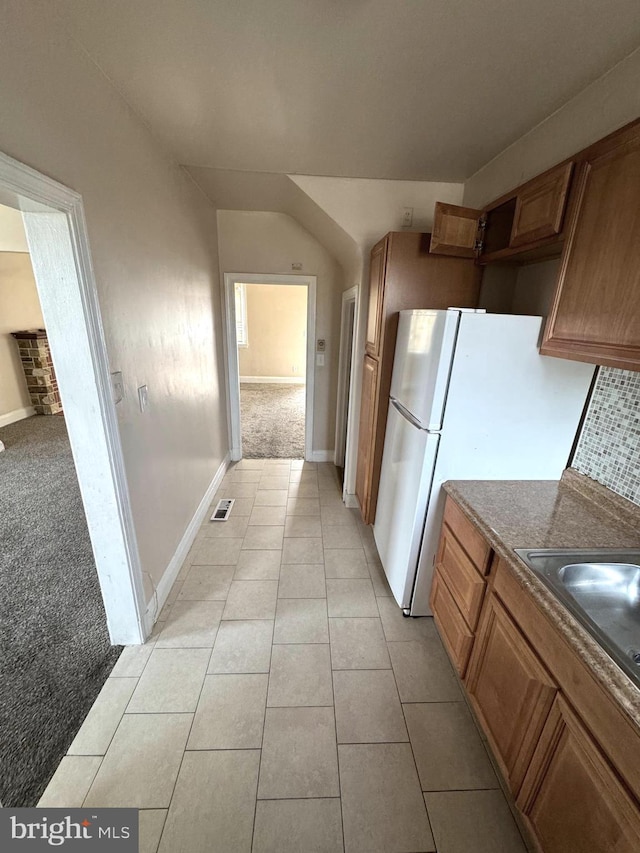 kitchen featuring brown cabinets, light tile patterned floors, visible vents, decorative backsplash, and light carpet