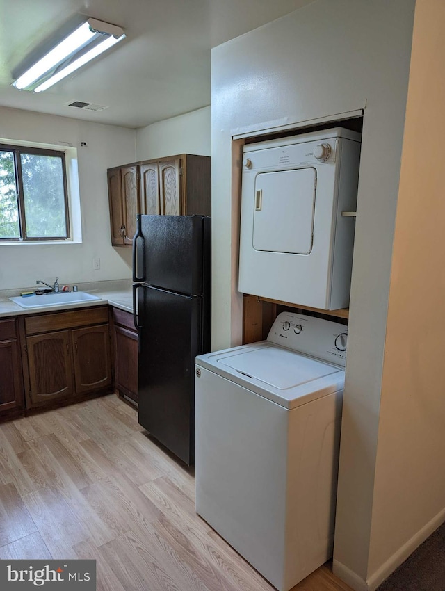 clothes washing area with sink, stacked washer / drying machine, and light wood-type flooring