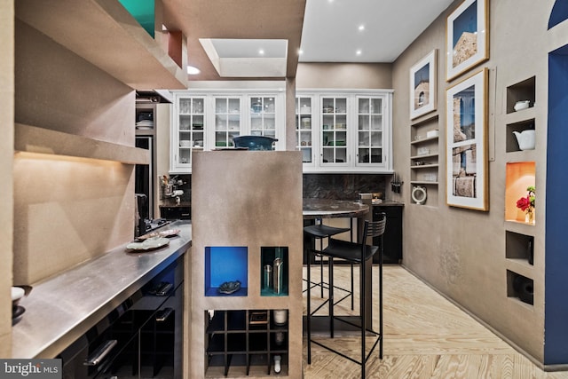 interior space with recessed lighting, stainless steel counters, glass insert cabinets, white cabinetry, and dark cabinetry