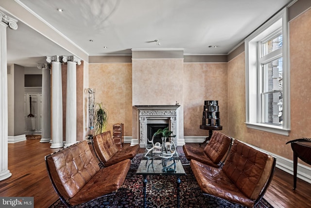 living area with decorative columns, baseboards, ornamental molding, dark wood-type flooring, and a fireplace