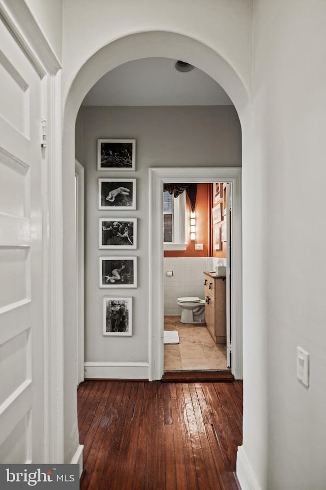 hallway featuring arched walkways, wood-type flooring, and baseboards