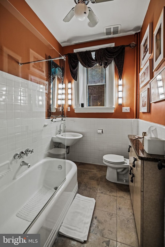 full bath featuring tile walls, visible vents, toilet, a sink, and shower / tub combination