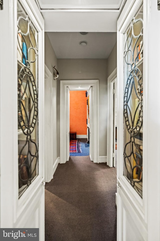 hall featuring dark carpet and baseboards