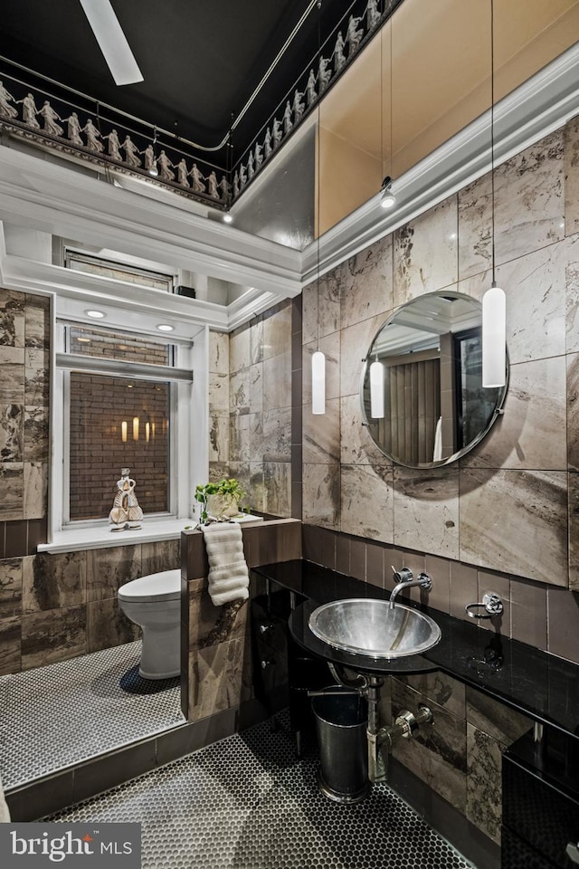 bathroom with a sink, toilet, and tile walls