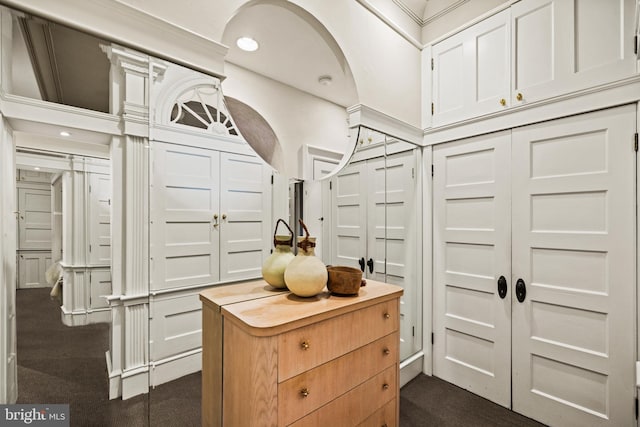 walk in closet with arched walkways and dark colored carpet