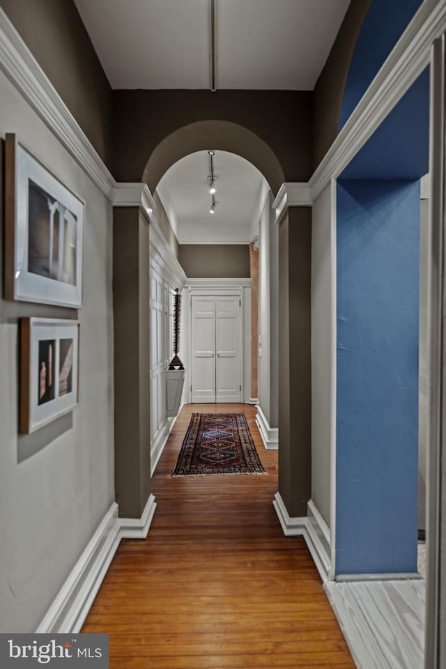 corridor featuring baseboards, arched walkways, and wood finished floors