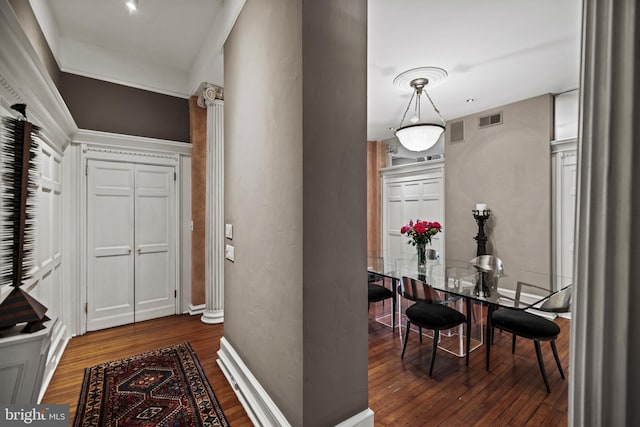 hallway with dark wood-style flooring, visible vents, baseboards, and ornate columns