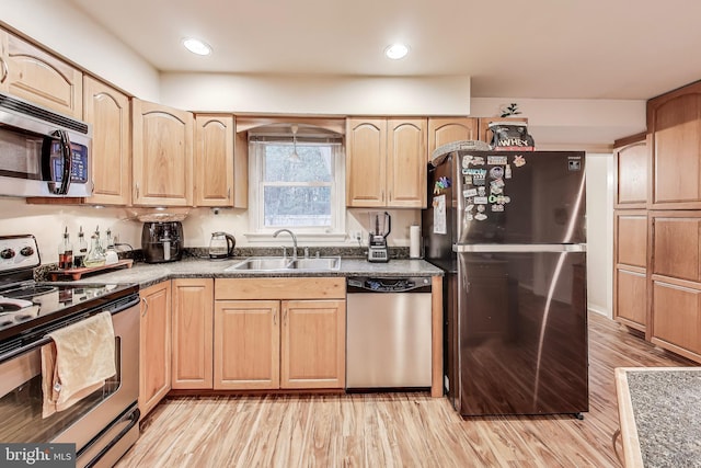 kitchen with appliances with stainless steel finishes, dark countertops, a sink, and light brown cabinetry