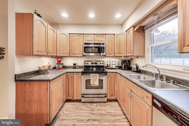 kitchen featuring stainless steel appliances, dark countertops, recessed lighting, light brown cabinetry, and a sink