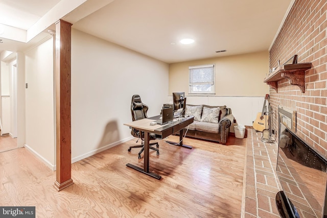 interior space with light wood-style floors, baseboards, a brick fireplace, and visible vents