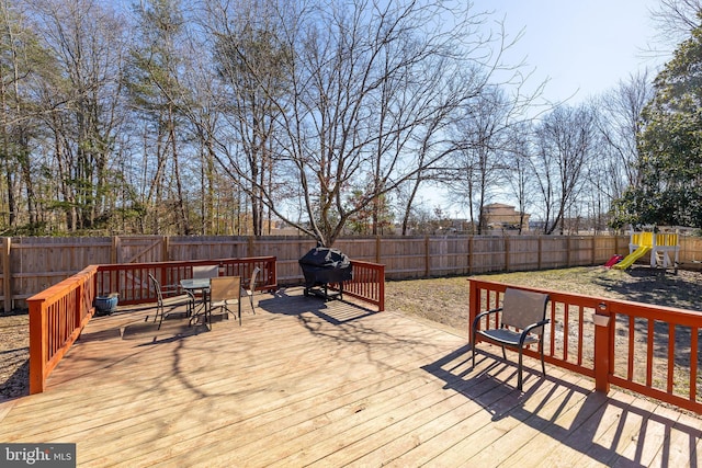 wooden terrace with outdoor dining space, a playground, a fenced backyard, and grilling area