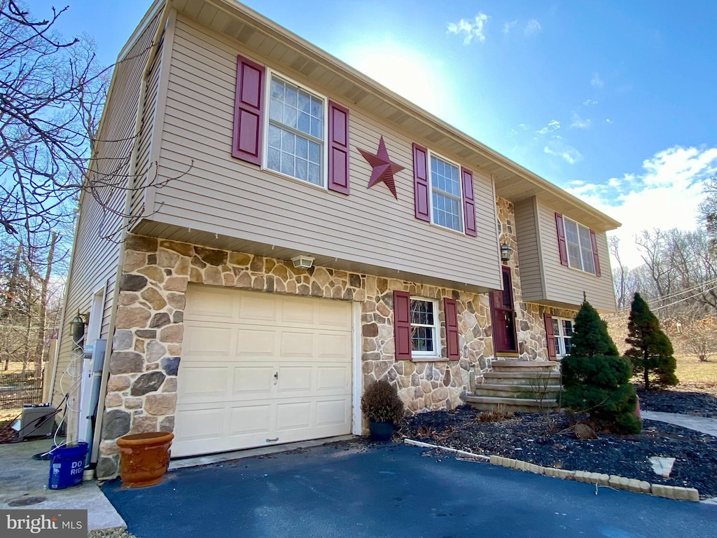 view of front of home with a garage, stone siding, and driveway