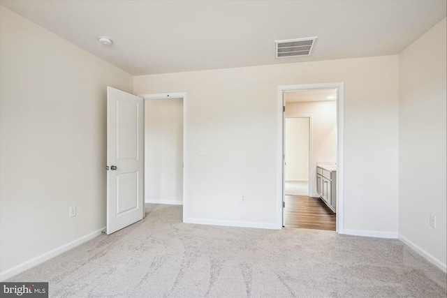 unfurnished bedroom featuring ensuite bath and light colored carpet