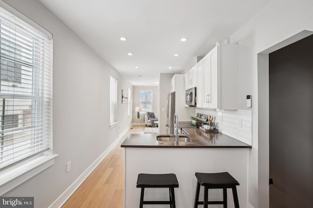 kitchen featuring appliances with stainless steel finishes, white cabinets, decorative backsplash, sink, and kitchen peninsula