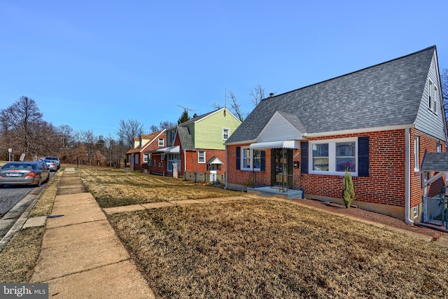 view of front of house featuring a residential view, brick siding, roof with shingles, and a front yard