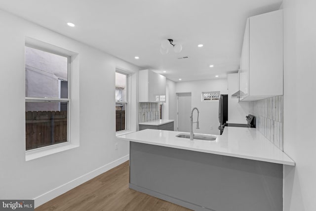 kitchen with sink, stove, white cabinets, kitchen peninsula, and light wood-type flooring