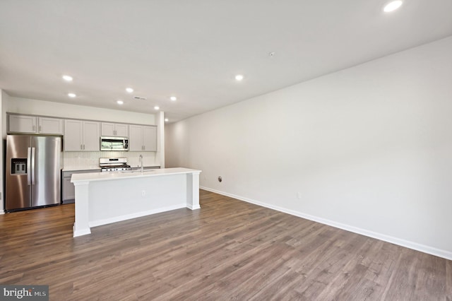 kitchen featuring sink, appliances with stainless steel finishes, a kitchen island with sink, backsplash, and dark hardwood / wood-style floors